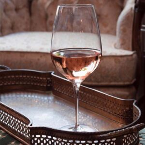 Glass of pink wine on a copper tray with a pink chair in the background.