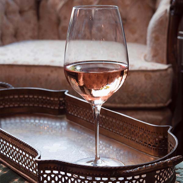 Glass of pink wine on a copper tray with a pink chair in the background.