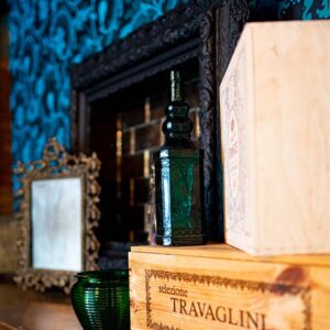 Green glass bottles and wooden wine boxes on a fireplace mantel.
